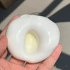 A hand holds a white, squishy stress relief ball with a yellow center.
