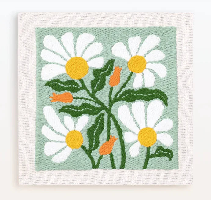 A punch needle embroidery kit featuring a light green background with white and yellow daisy flowers and orange stems.