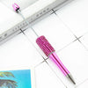 A pink beaded ballpoint pen craft kit with a silver tip rests on a white surface next to a book.
