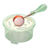 A clear container of wax is shown with a metal spoon and wooden handle for melting wax.