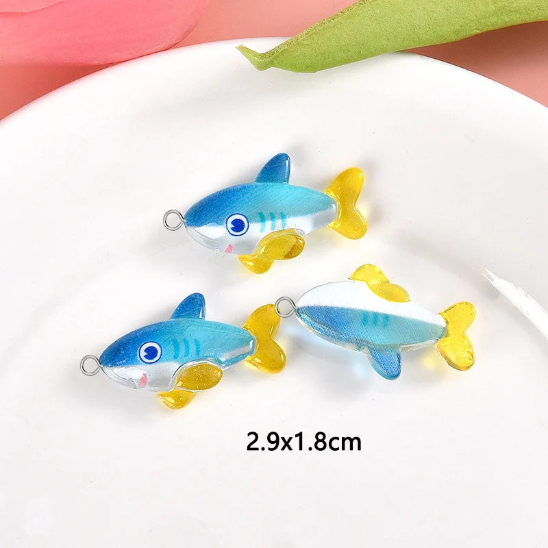 Two small blue and yellow fish resin charms displayed on a white plate.