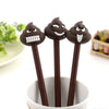 A pack of three dark brown novelty cartoon poop gel pens standing upright in a white cup.
