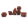 A set of seven polyhedral dice in shades of reddish-brown and amber resting on a white surface.