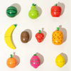A collection of wooden magnetic fruit shapes including a green apple, yellow banana, red tomato, and orange pumpkin.
