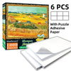 Box of a 1000-piece jigsaw puzzle featuring a rural landscape with fields and buildings, including adhesive paper sheets.