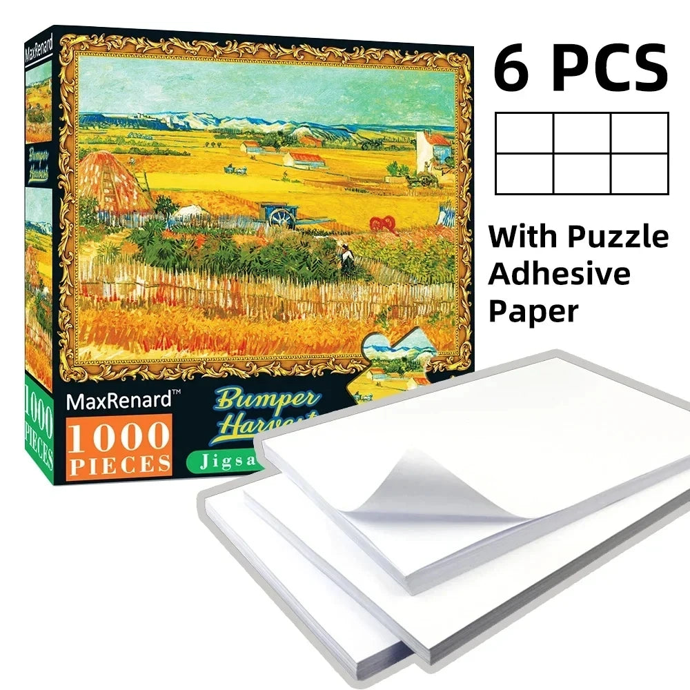 Box of a 1000-piece jigsaw puzzle featuring a rural landscape with fields and buildings, including adhesive paper sheets.