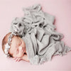 A newborn baby sleeping peacefully wearing a knit wrap and a pearl headband on a pink background.