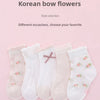 A selection of five pairs of light pink and white floral cotton socks displayed on a pink background.