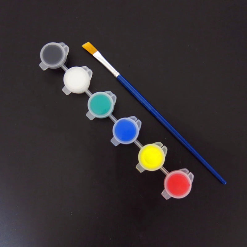 A set of twelve colored acrylic paint droppers and a brush arranged in a line on a dark surface.