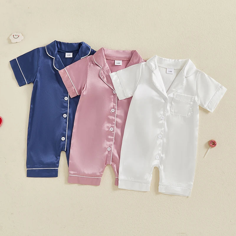 Three satin button-up rompers in navy blue, pink, and white laid out on a light background.