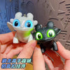 A hand holds a Toothless dragon keychain featuring movable wings and glowing green eyes against a light background.