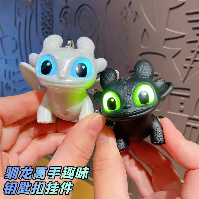 A hand holds a Toothless dragon keychain featuring movable wings and glowing green eyes against a light background.