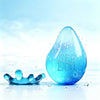 A clear blue teardrop shaped squishy toy with the text NEED DOT is surrounded by water droplets.