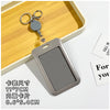 A gray retractable ID badge holder with a clip is shown on a wooden tray next to a keychain.