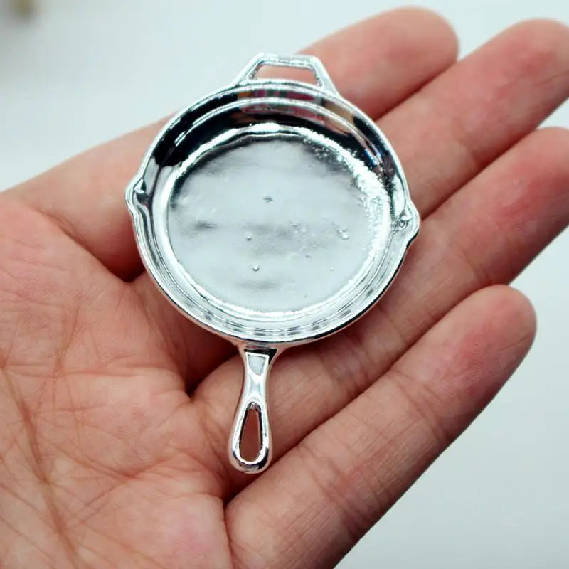 A small, silver-colored miniature copper soup pot with a handle is held in a person's hand.