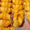 A hand holds a golden yellow squishy croissant stress relief toy with visible layers and orange glaze.