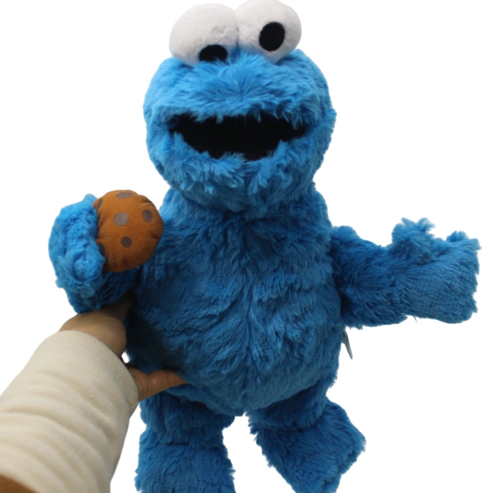 A blue Cookie Monster plush toy with large eyes and a hand holding an orange cookie.
