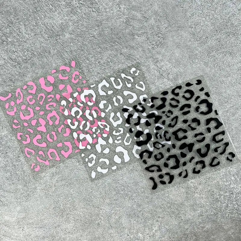 A transparent decal featuring a leopard print pattern in shades of pink, white, and black on a gray surface.