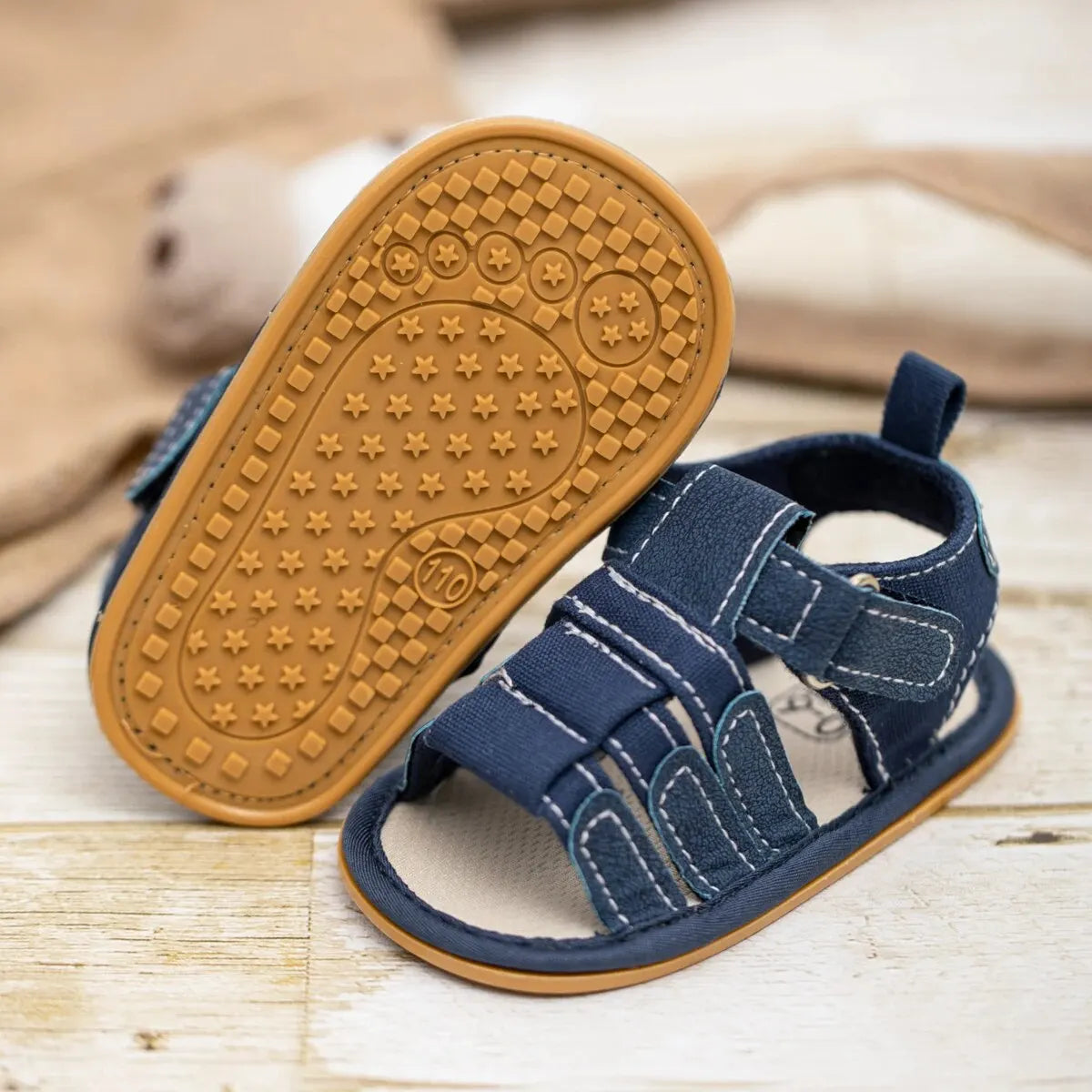 A pair of soft blue non-slip baby sandals for first walkers resting on a wooden surface.
