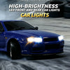 A blue Nissan Skyline R34 drift car with bright LED headlights driving on a road.