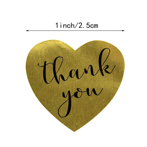 A heart-shaped gold sticker with the text thank you written in black script.