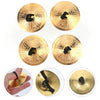Four gold-colored mini copper finger cymbals shown in various views and a hand for scale