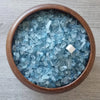 A wooden bowl filled with blue aquamarine chips and a small white crystal.
