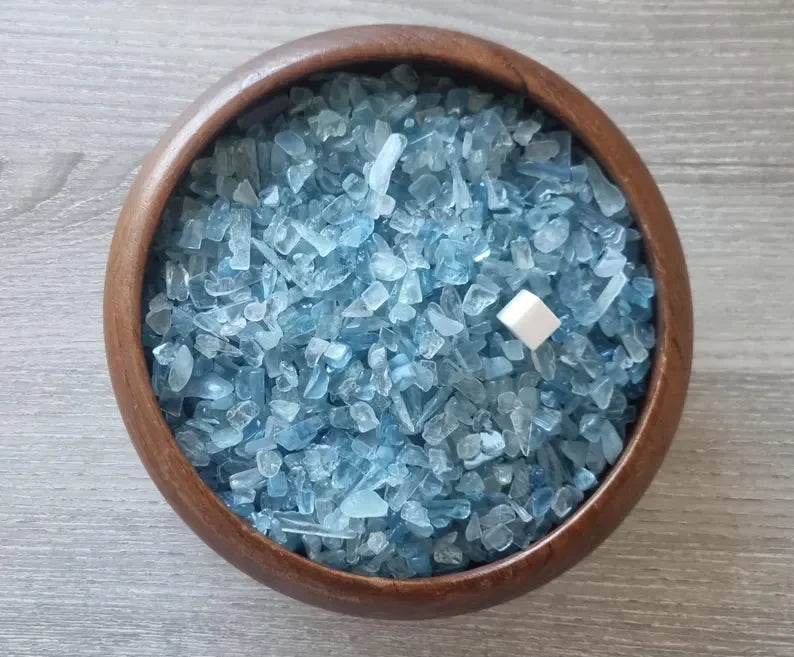A wooden bowl filled with blue aquamarine chips and a small white crystal.