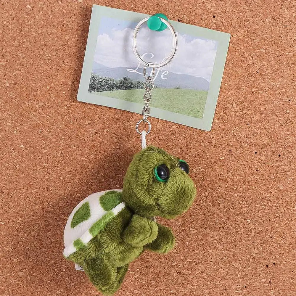 A green turtle plush charm attached to a silver keyring, displayed against a card.
