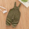 Olive green baby cotton overalls with adjustable straps lying on a wooden surface.