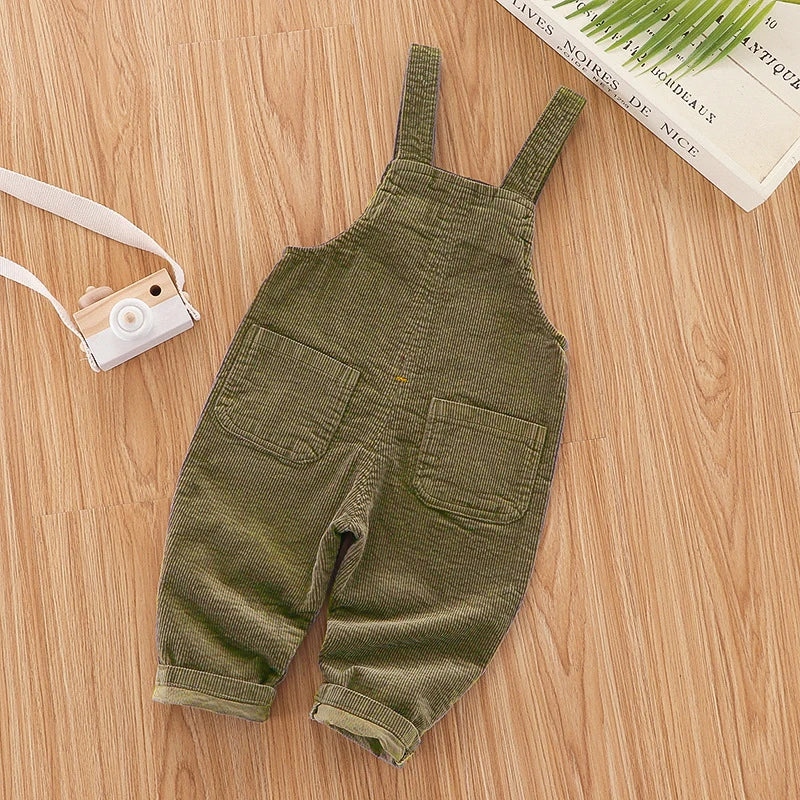 Olive green baby cotton overalls with adjustable straps lying on a wooden surface.