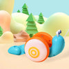 An orange and light blue musical pull-along snail toy is shown on a light surface with green trees in the background.