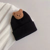 A knitted black baby hat with a brown teddy bear ear on a white background.