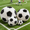 A collection of white and black plush soccer balls resting on a green football field.