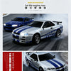 A silver and blue 1/18 scale Nissan GT-R R34 drift car is shown in motion on a track.