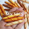 A hand holds five miniature baguette-shaped crackers on a white surface.