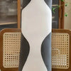 A plush cat pillow resembling a black and white cat is sitting upright on a brown leather sofa.
