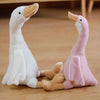 A white and pink long neck goose plush doll sitting on a wooden floor.
