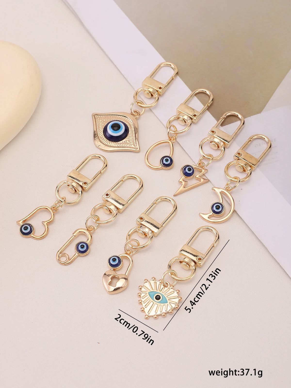 A set of gold-toned evil eye keychains featuring blue eyes and various shapes for bags and backpacks.