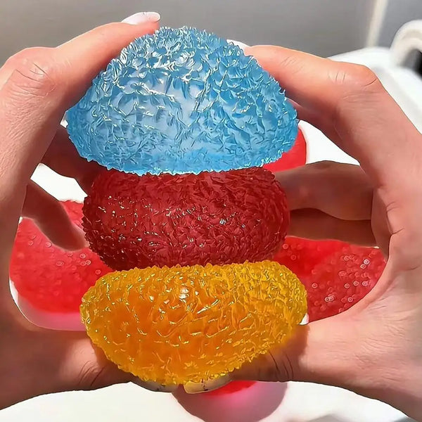 Three soft squeeze sensory balls in blue, red, and yellow held in a person's hands.
