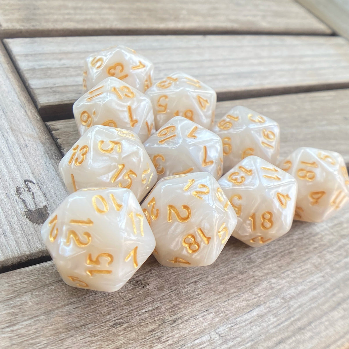 A collection of ten translucent pearl acrylic D20 dice showing various numbered faces on a wooden surface.