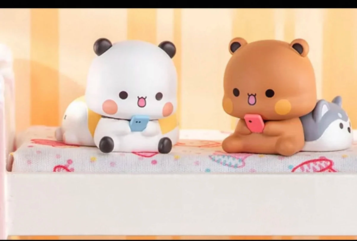 Un par de figuras coleccionables de caja ciega, un panda blanco y un oso marrón, sentados sobre una superficie clara.