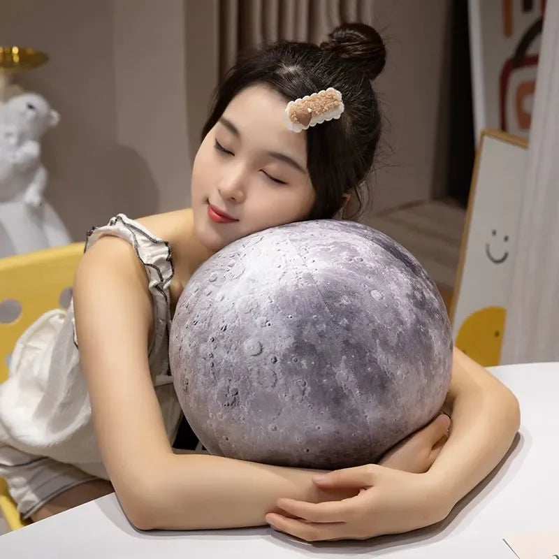 A woman is holding a large, spherical gray plush toy resembling the moon, with a small white piece on top.