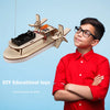 A boy proudly holds a DIY wooden paddle boat kit made of wood and plastic components.