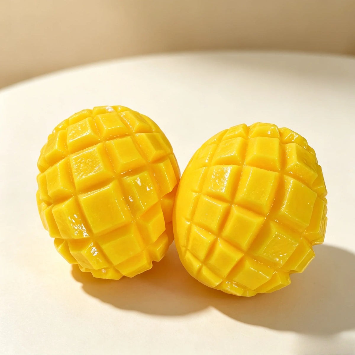 Two bright yellow mango squishy stress relief balls with a crispy texture are shown on a light surface.
