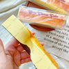 A yellow butter stick squishy toy is held in a hand next to packaged cheese take products.