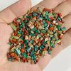 A hand holds a pile of natural tumbled stone chips in various shades of green, orange, and brown.
