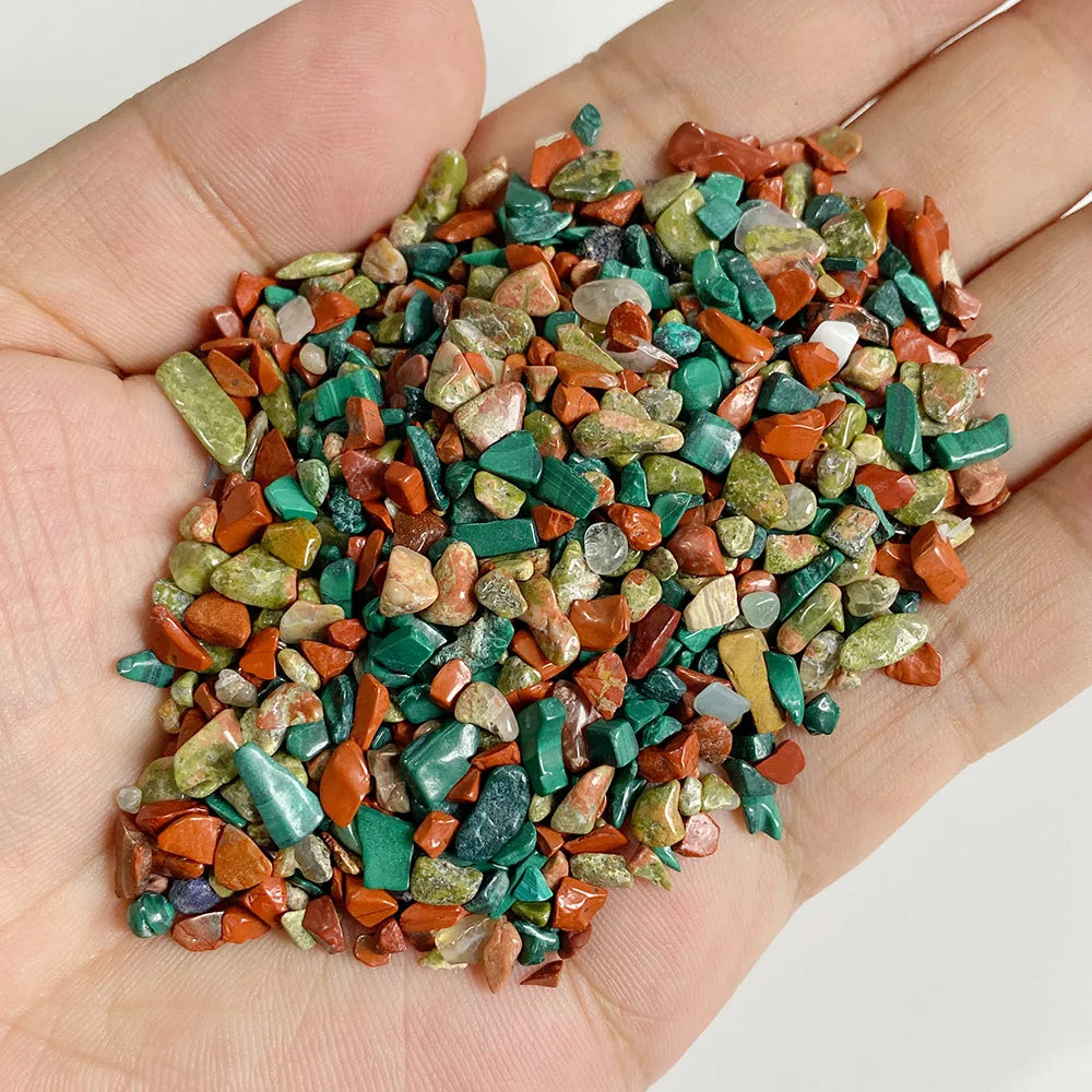 A hand holds a pile of natural tumbled stone chips in various shades of green, orange, and brown.