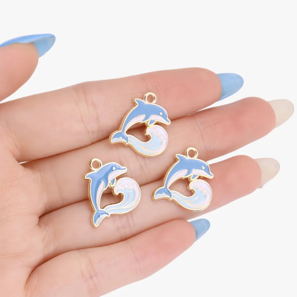 Gold enamel marine life charms shaped like dolphins and waves displayed on a hand
