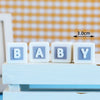 White cube letter toys spelling BABY on a light blue wooden surface